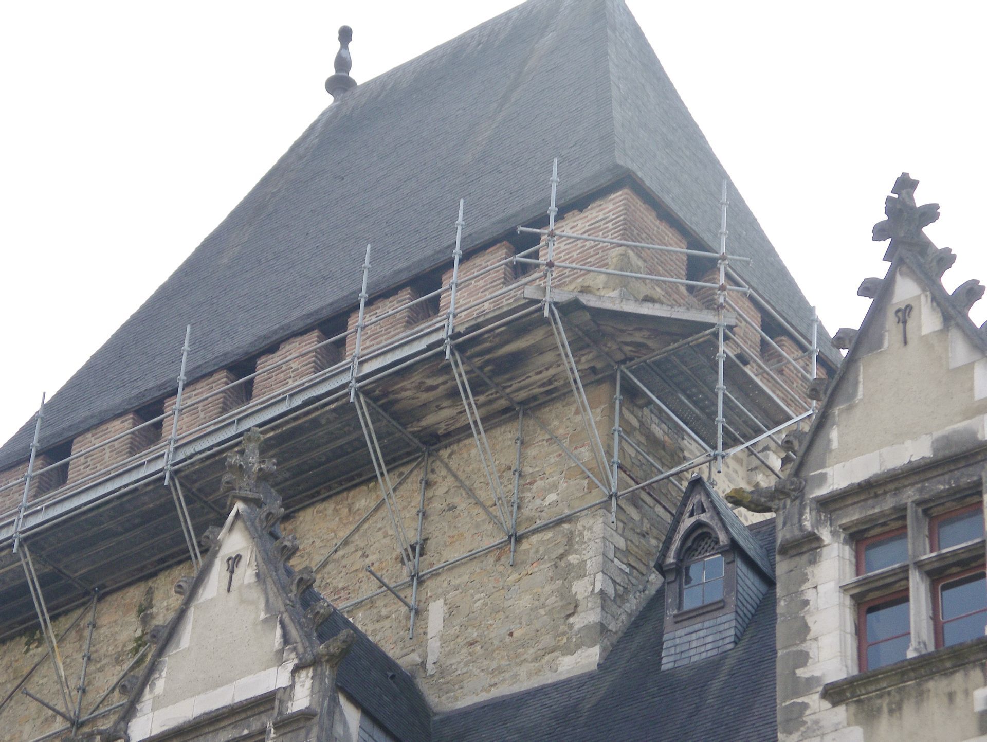 Échafaudages sur un bâtiment en pierre au toit de tuiles sombres.