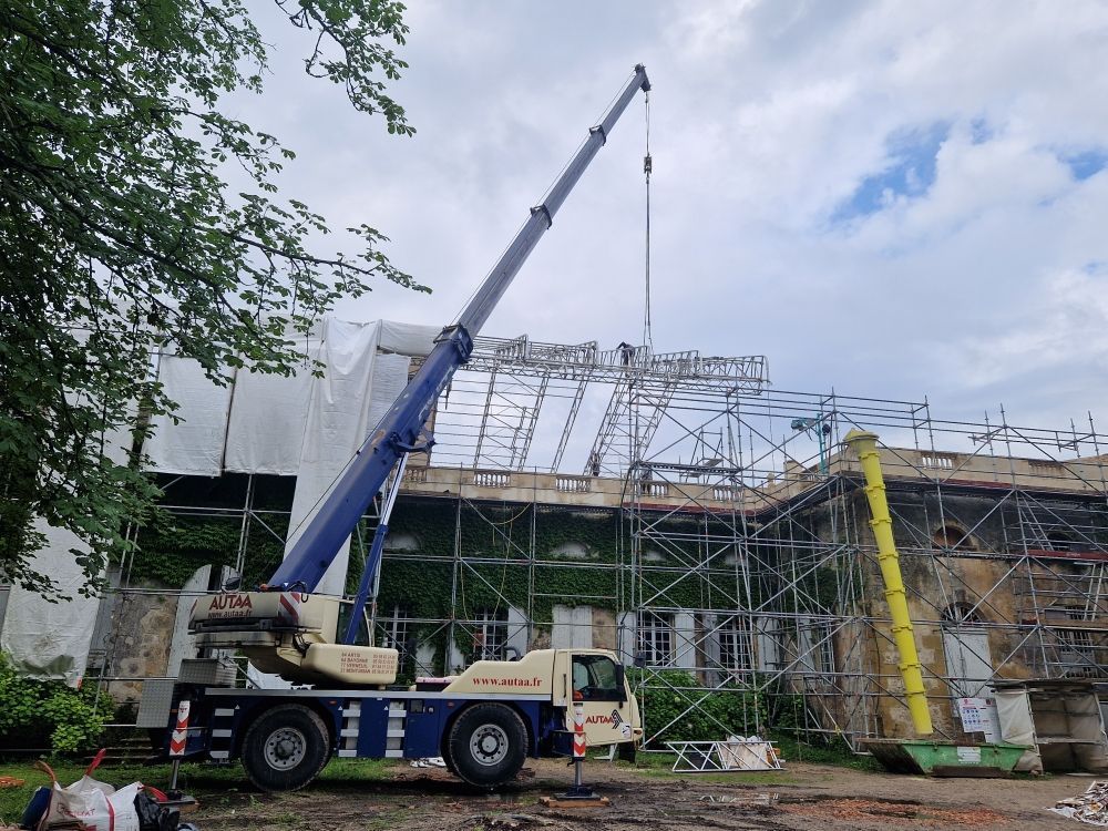 Une grue soulève un échafaudage métallique sur un bâtiment en rénovation.
