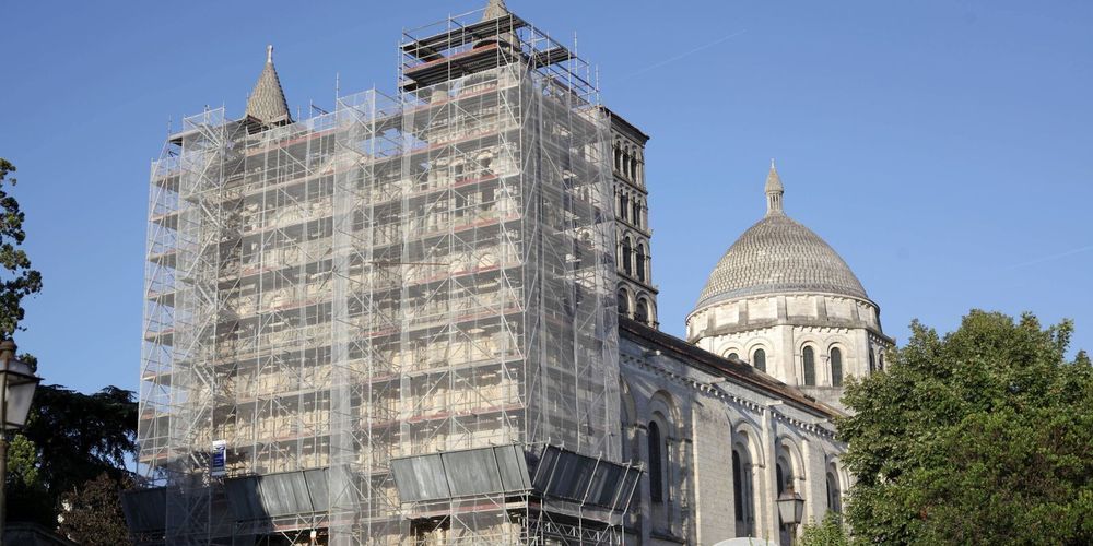 Église en pierre avec échafaudages et dôme.