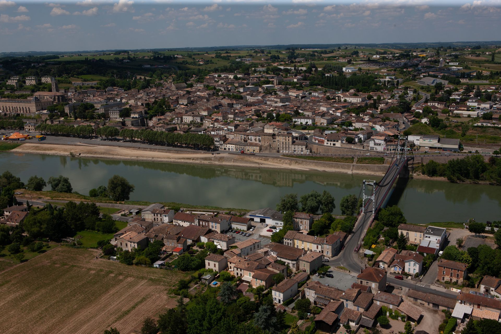 Vue aérienne de La Réole avec une rivière, un pont et des champs verdoyants.