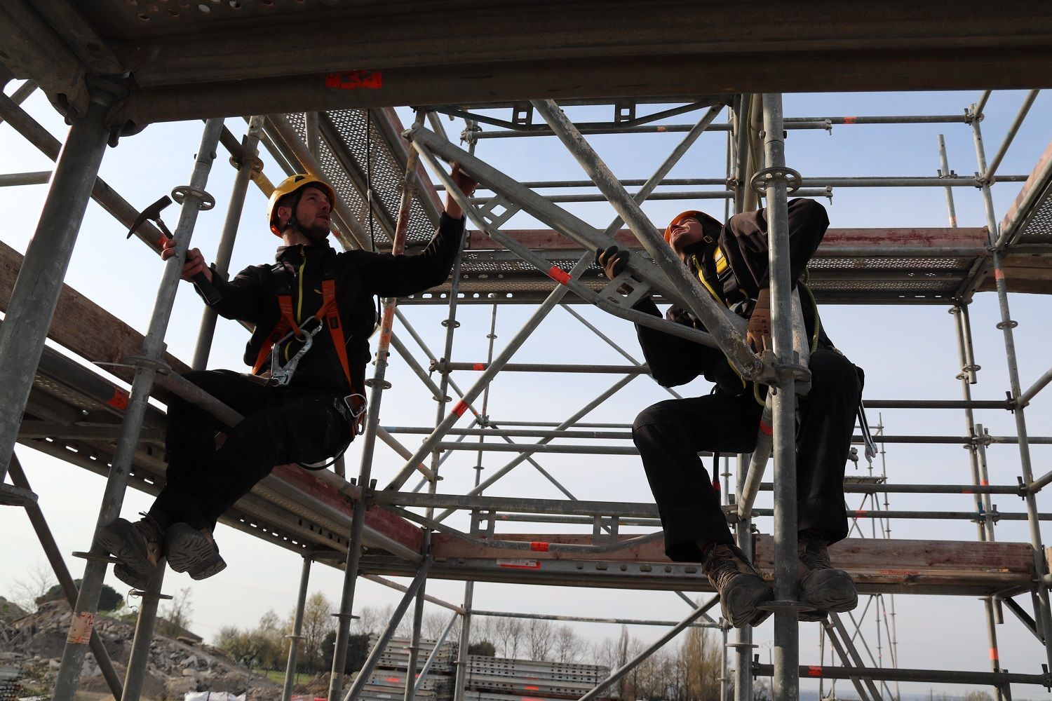 Deux ouvriers harnachés construisent un échafaudage.