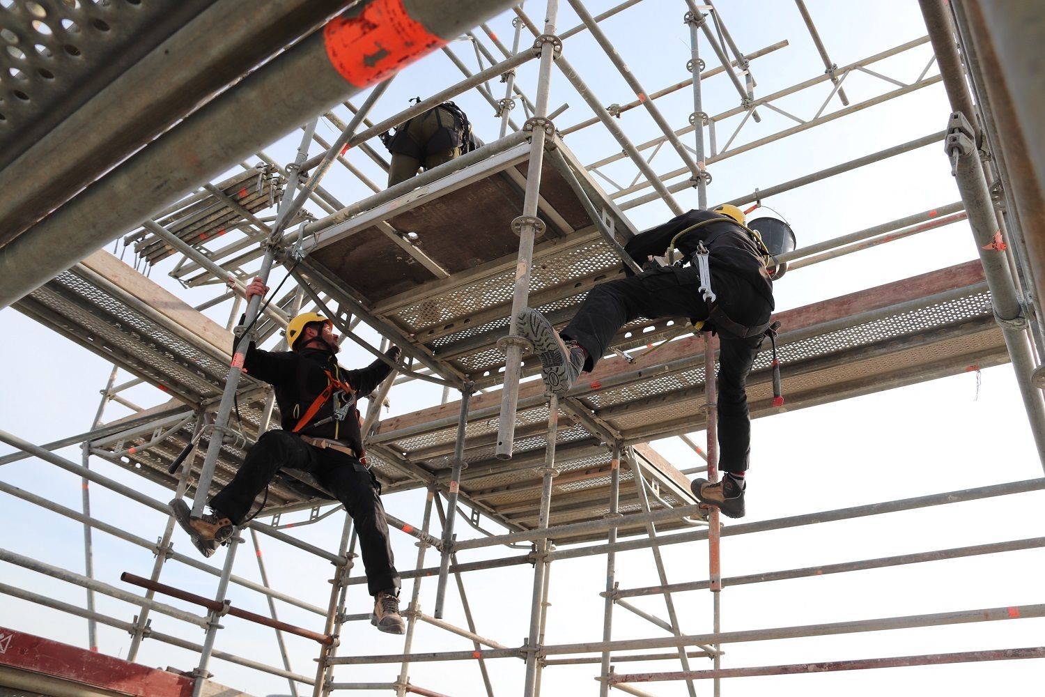 Deux personnes harnachées escaladent une structure métallique d'échafaudage.