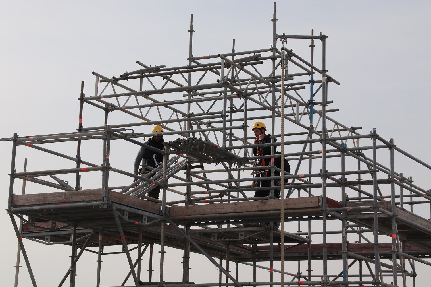 Deux ouvriers sur un échafaudage, en train de construire une structure métallique.