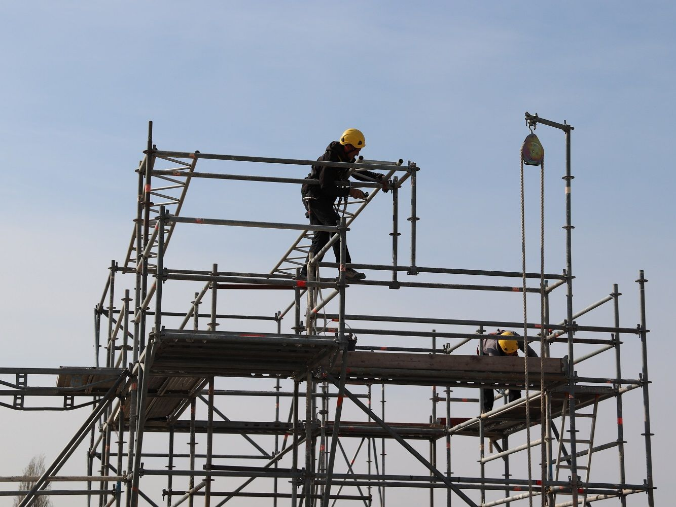 Une personne portant un casque de chantier jaune travaille sur un échafaudage métallique.
