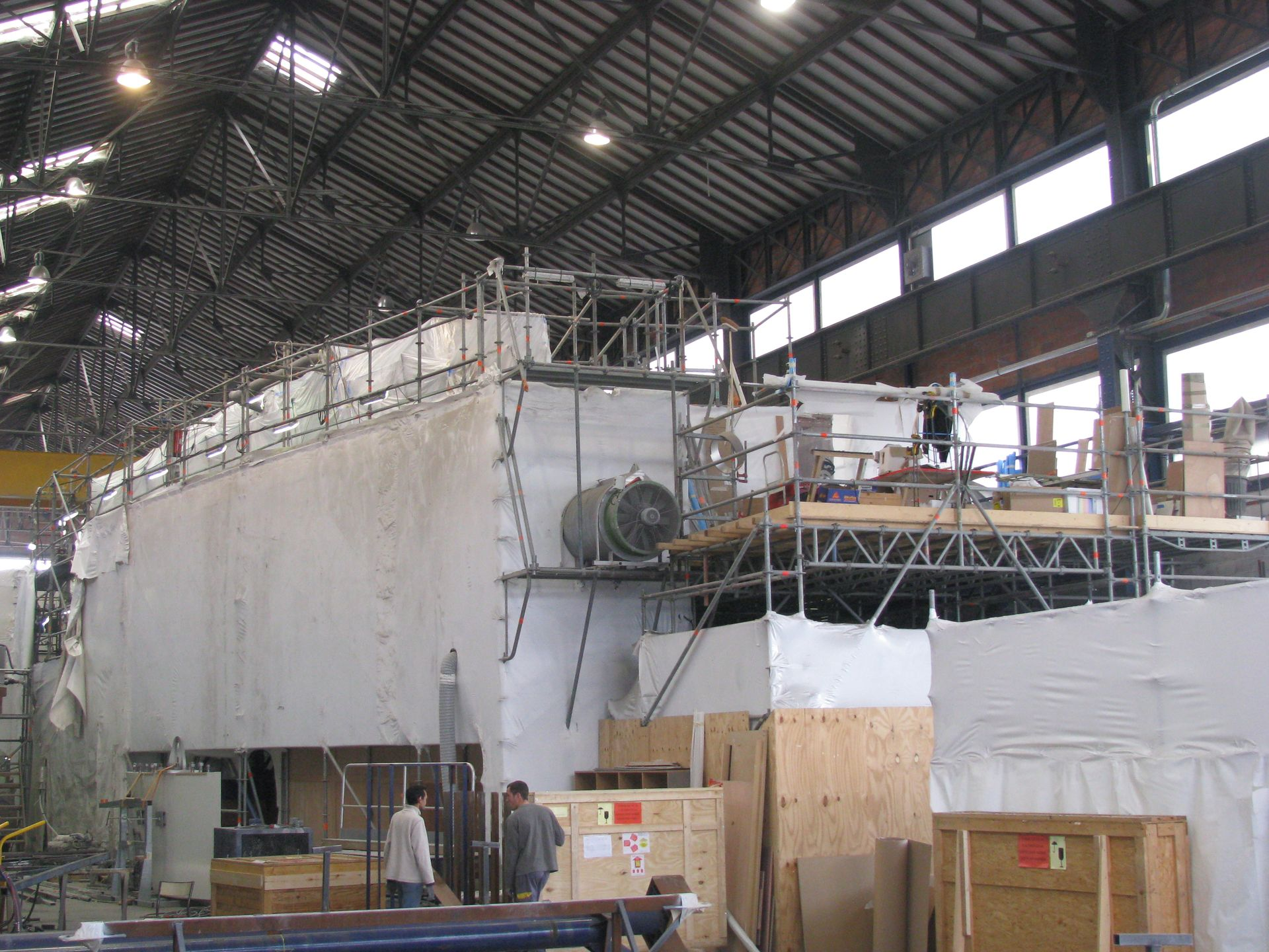 Imposante structure industrielle dans un entrepôt, recouverte de blanc. Échafaudages visibles.