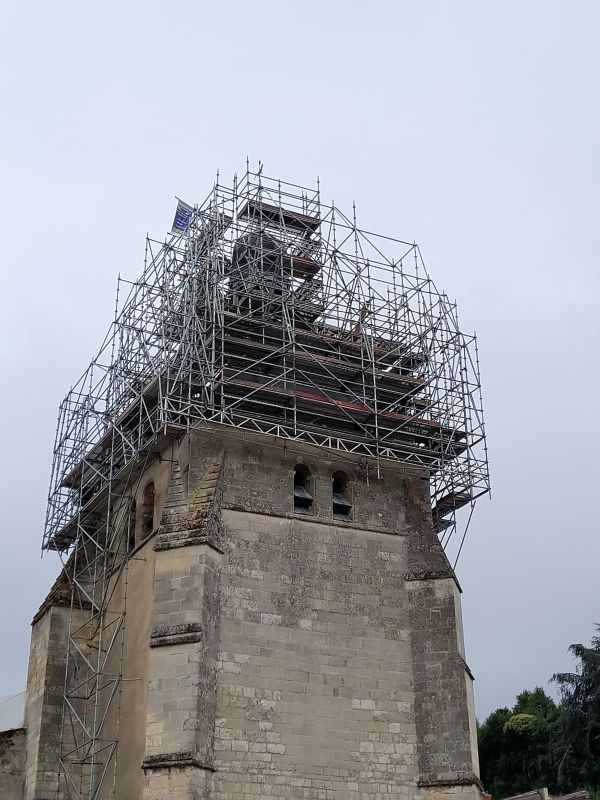 Des échafaudages entourent le clocher en pierre d'une église, en cours de réparation.
