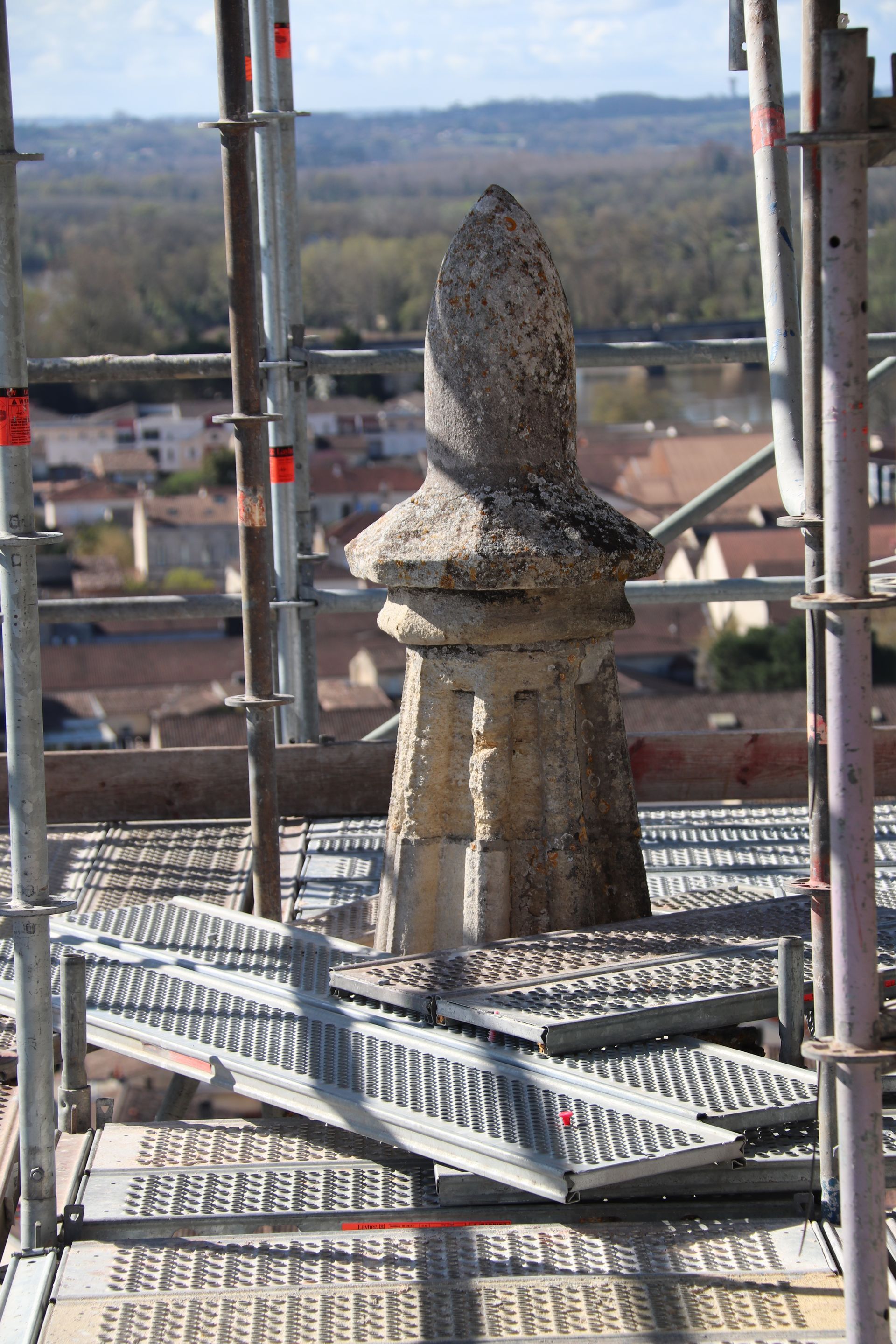 Flèche de pierre sur échafaudage en cours de restauration avec une ville en arrière-plan.