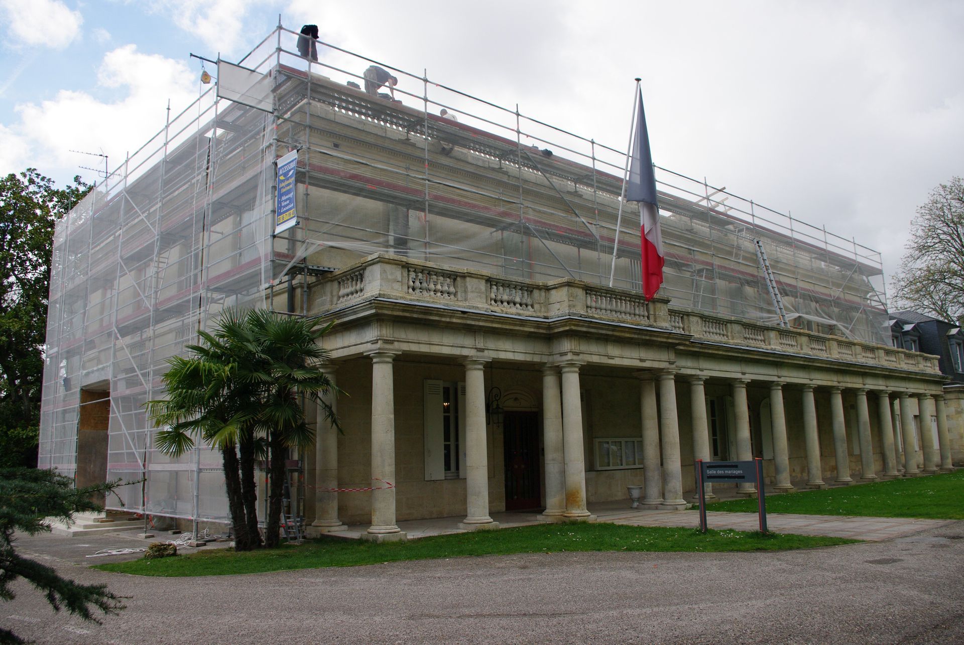 Bâtiment en rénovation, recouvert d'échafaudages et de filets, avec un drapeau français.