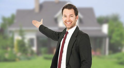 Un agent immobilier montre une maison en souriant.