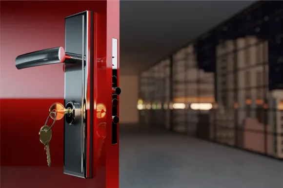 Puerta roja parcialmente abierta, revelando una manija cromada con llaves y una ciudad borrosa por la noche.