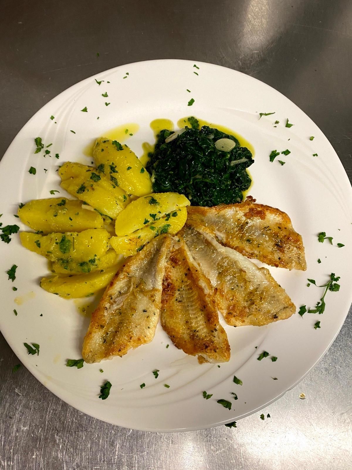 Teller mit gebratenen Fischfilets, Kartoffeln und Spinat, garniert mit Petersilie.