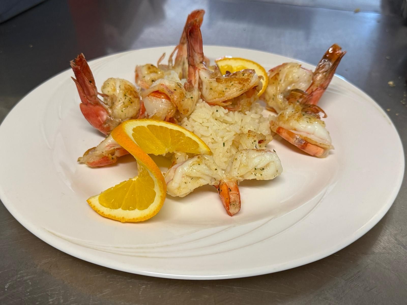 Gegrillte Garnelen mit Reis und Orangenscheiben auf einem weissen Teller.