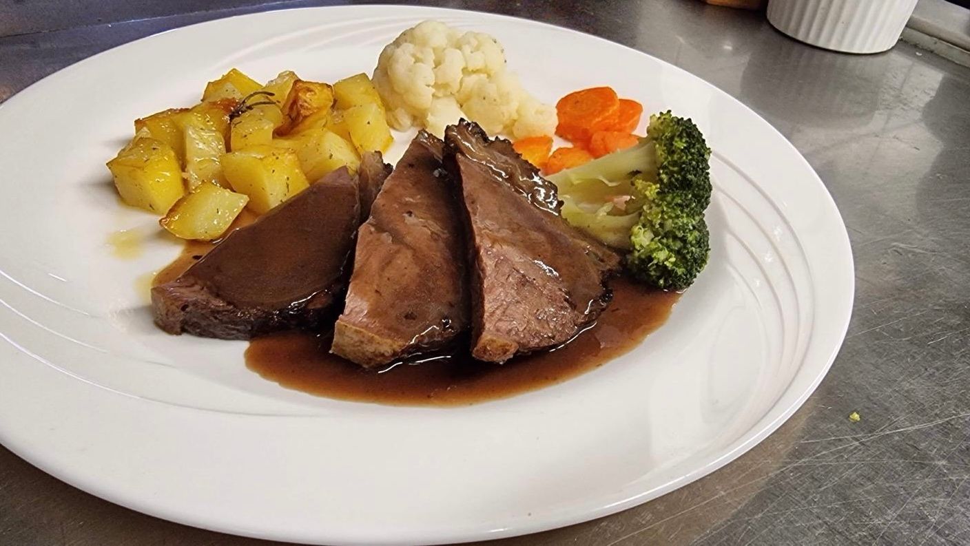 In Scheiben geschnittenes Roastbeef mit Sosse, Bratkartoffeln und Gemüse auf einem weissen Teller.