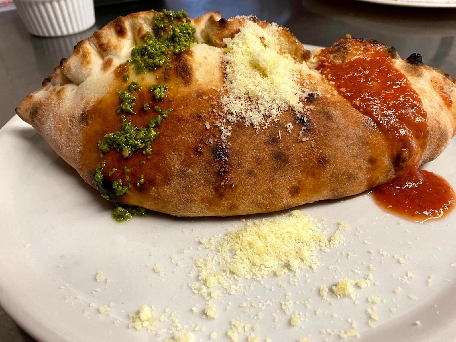 Calzone mit Pesto und Tomatensauce, mit geriebenem Käse bestreut, auf einem weissen Teller.