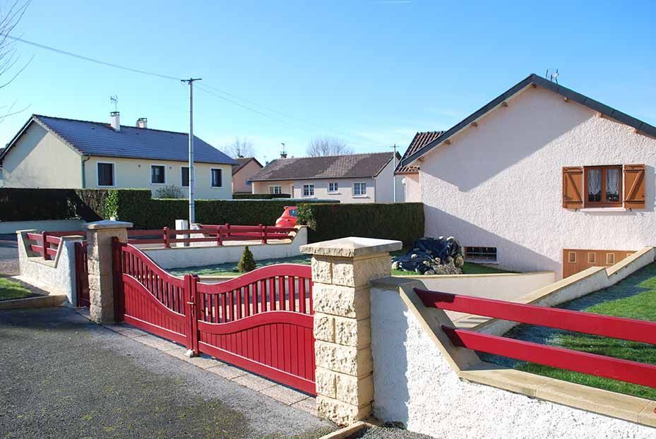 Portail rouge et mur de pierre devant des maisons de banlieue par une journée ensoleillée