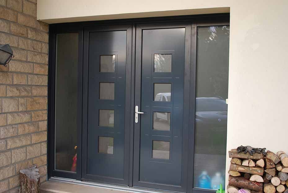 Entrée principale avec double porte sombre, fenêtres à carreaux carrés et bois de chauffage empilé près du porche.