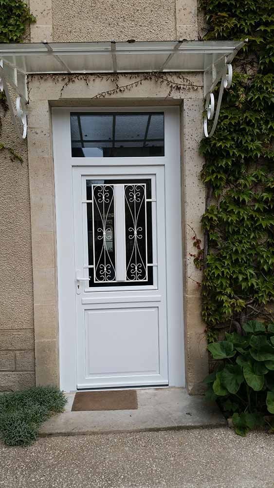 Porte d'entrée blanche avec panneaux de verre décoratifs, encastrée dans un porche en pierre et encadrée de lierre vert.