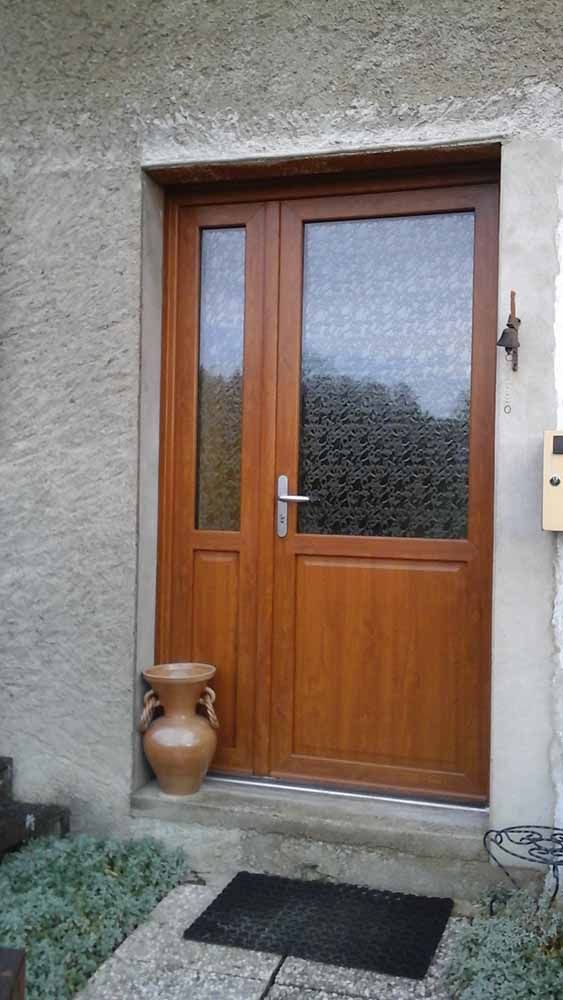 Porte d'entrée en bois avec panneau en verre dépoli, à côté d'un pot en terre cuite et d'un paillasson contre un mur en stuc.