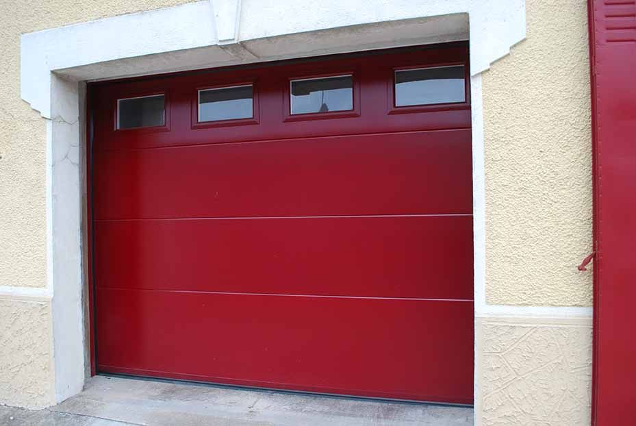 Porte de garage rouge avec de petites fenêtres sur une façade beige