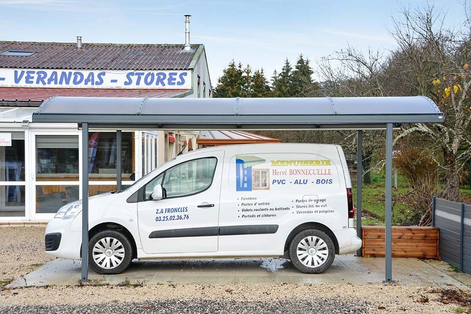 Fourgonnette de service blanche garée sous un auvent gris devant les magasins Verandas.