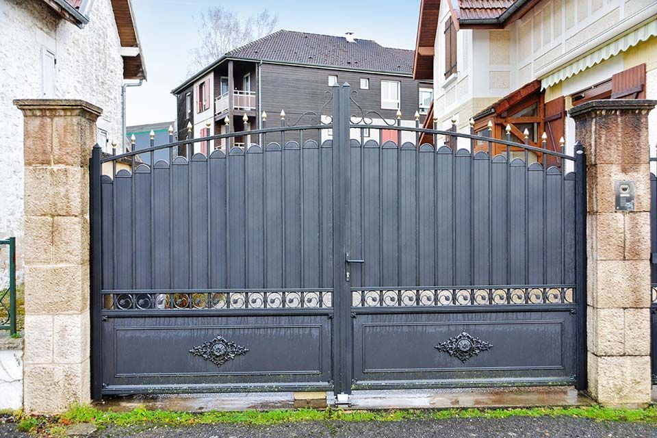 Portail d'allée double en métal gris entre des piliers en pierre devant une maison