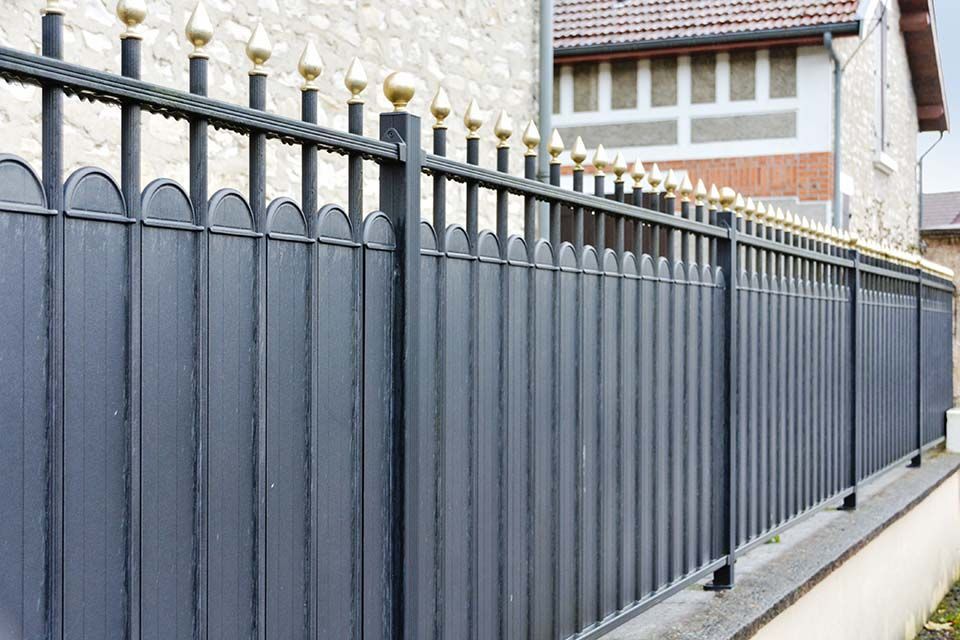 Clôture en métal gris foncé avec des poteaux à embouts dorés le long d'un trottoir bordant des maisons
