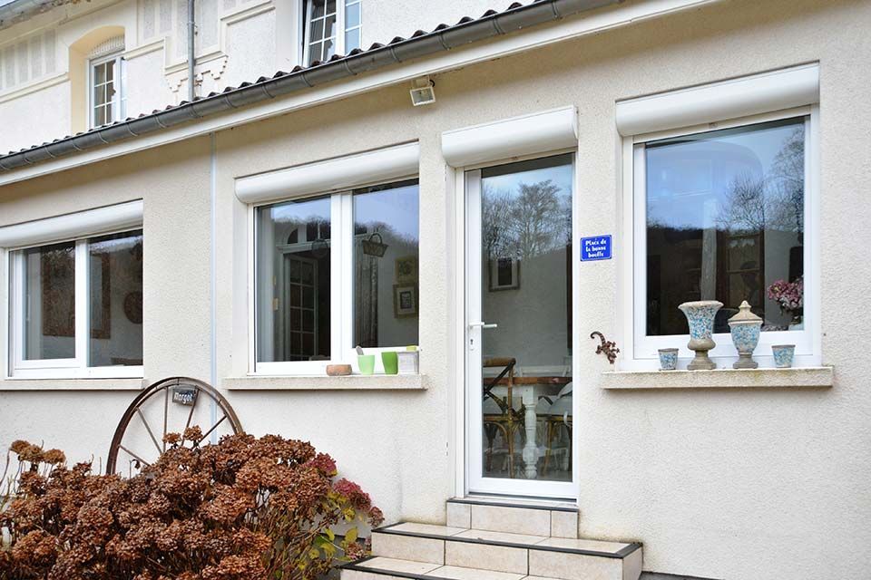 Façade de maison blanche avec fenêtres, porte vitrée et plantes en pot près de l'entrée