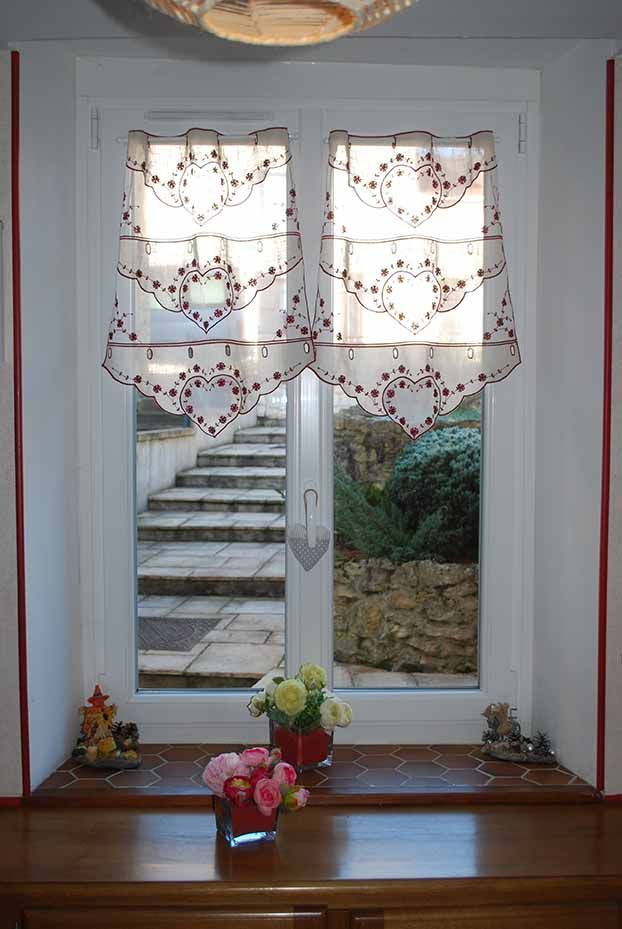 Fenêtre à rideaux décoratifs au-dessus d'une corniche en bois, avec des fleurs et un escalier visible à l'extérieur