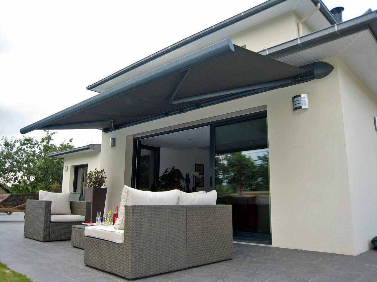 Terrasse moderne avec mobilier en osier gris devant une maison couleur crème, sous un grand auvent.