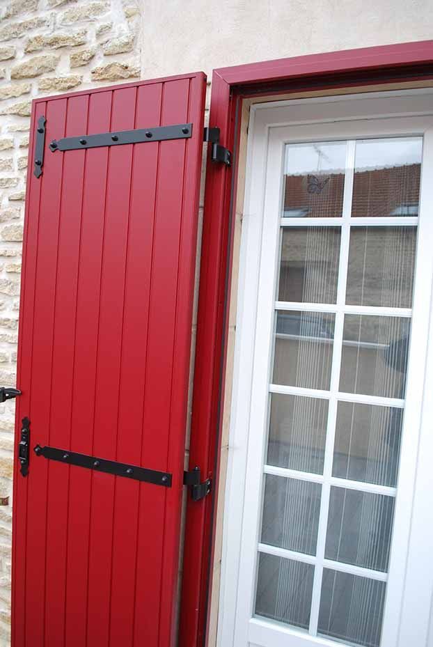Volet en bois rouge à côté d'une fenêtre à carreaux blancs sur un mur en pierre