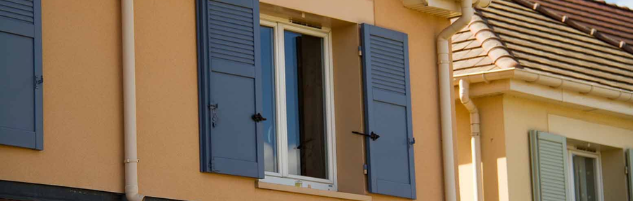 Volets bleus sur un bâtiment beige autour d'une fenêtre ouverte avec des rideaux