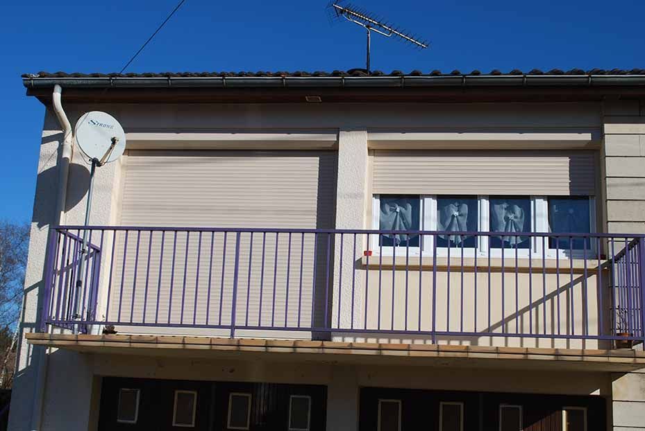 Façade d'une maison à deux étages avec balcon, volets fermés et antenne parabolique sous un ciel bleu