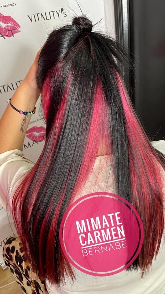 Una mujer con cabello negro y rojo lleva una camisa blanca.