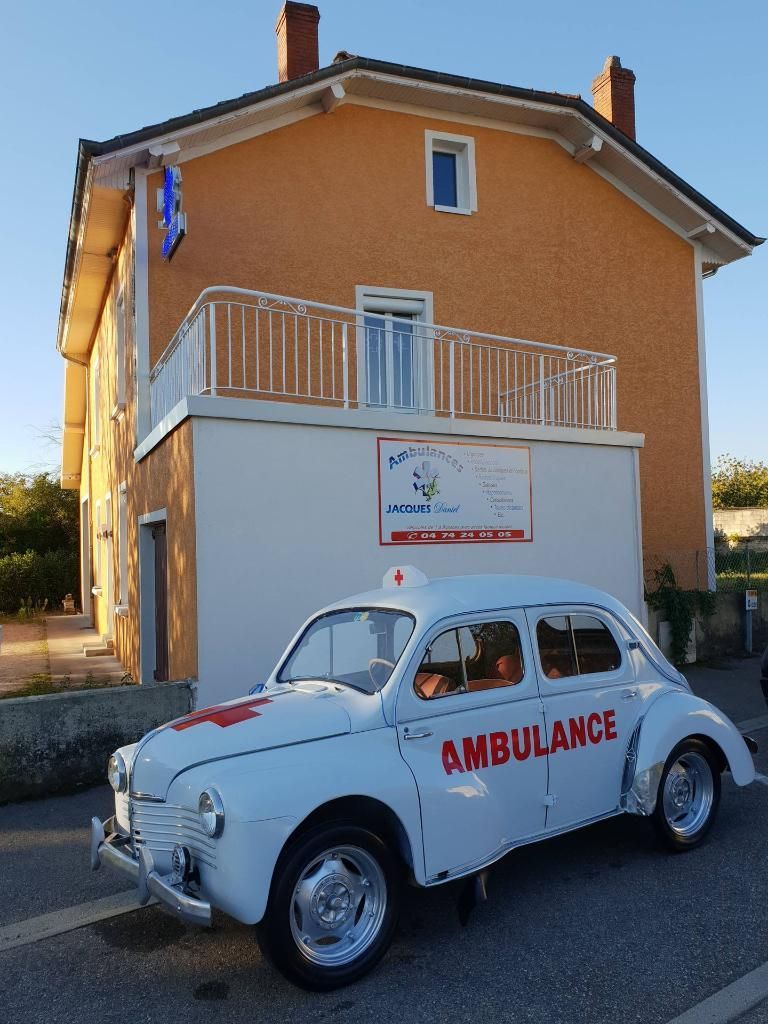 Une ambulance blanche d'époque garée devant un immeuble orange avec un balcon. L'ambulance porte des marquages ​​rouges.