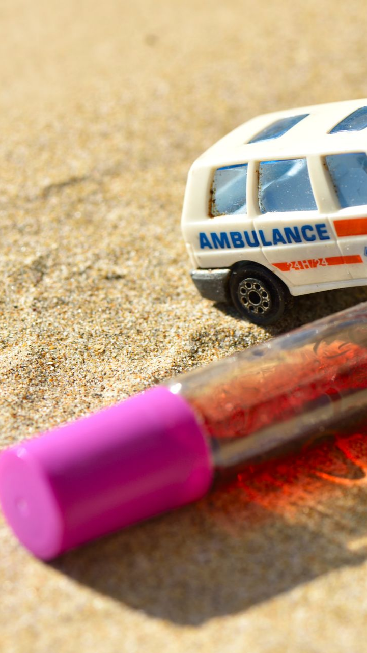 Ambulance miniature sur le sable ; tube sanguin au premier plan.
