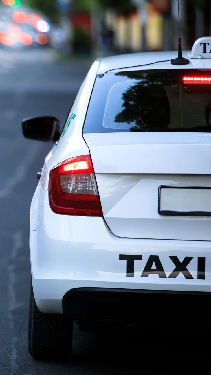 Vue arrière d'un taxi blanc dans une rue, avec l'inscription TAXI sur le dessus de la voiture.