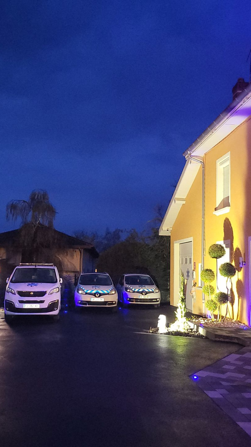 Trois voitures garées devant une maison jaune au crépuscule.