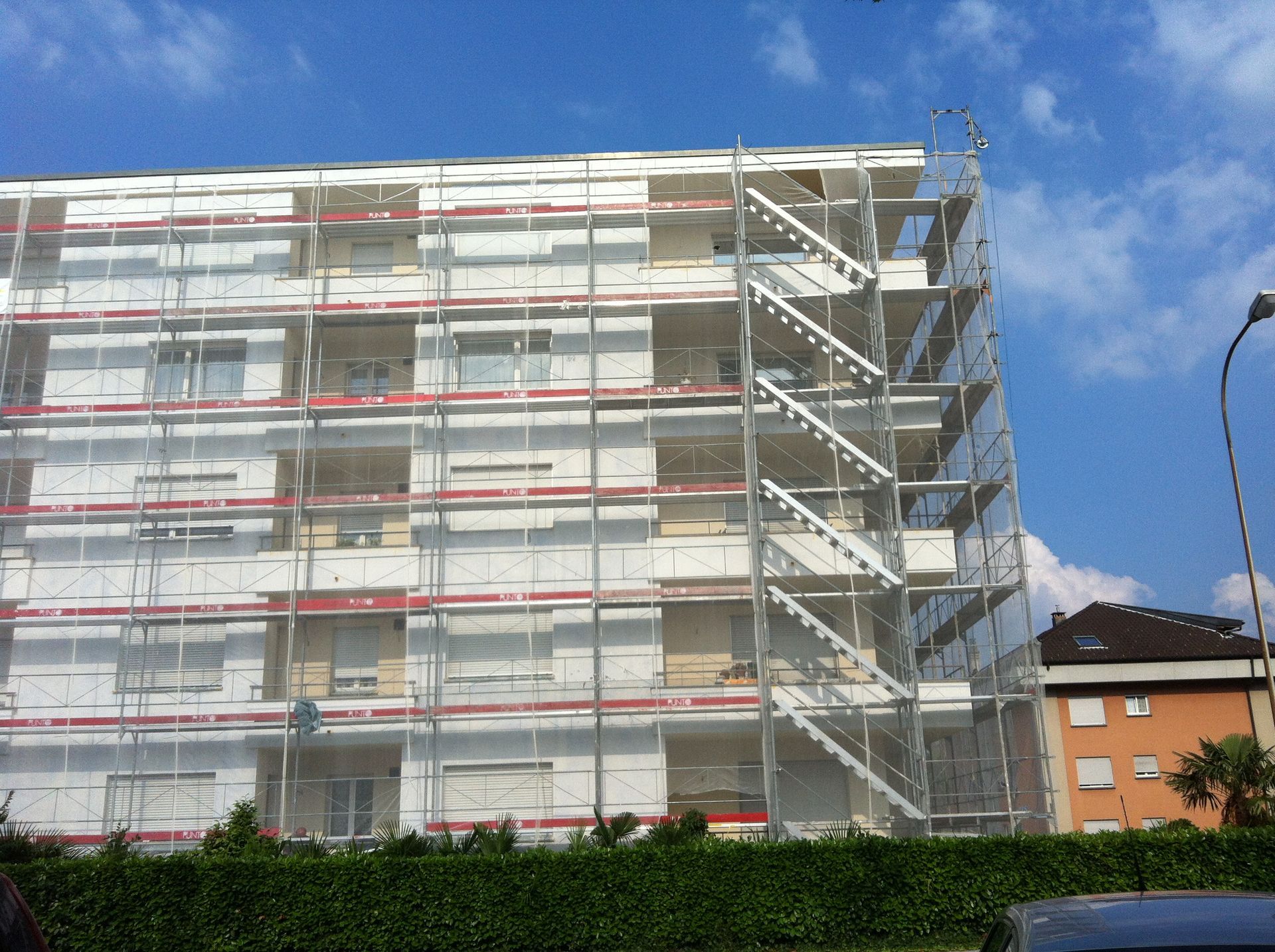 Edificio in costruzione con impalcature e reti di sicurezza, cielo azzurro sullo sfondo.
