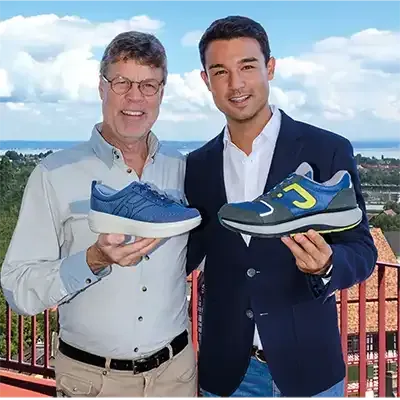 Zwei Männer stehen nebeneinander und halten Schuhe mit dem Buchstaben C darauf