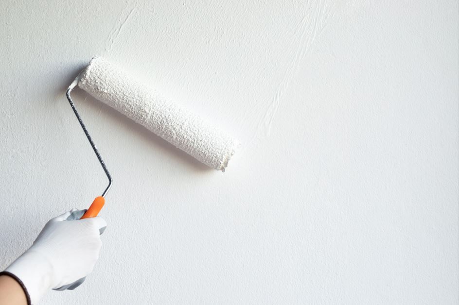Persona que lleva un guante pintando una pared blanca con un rodillo de pintura.