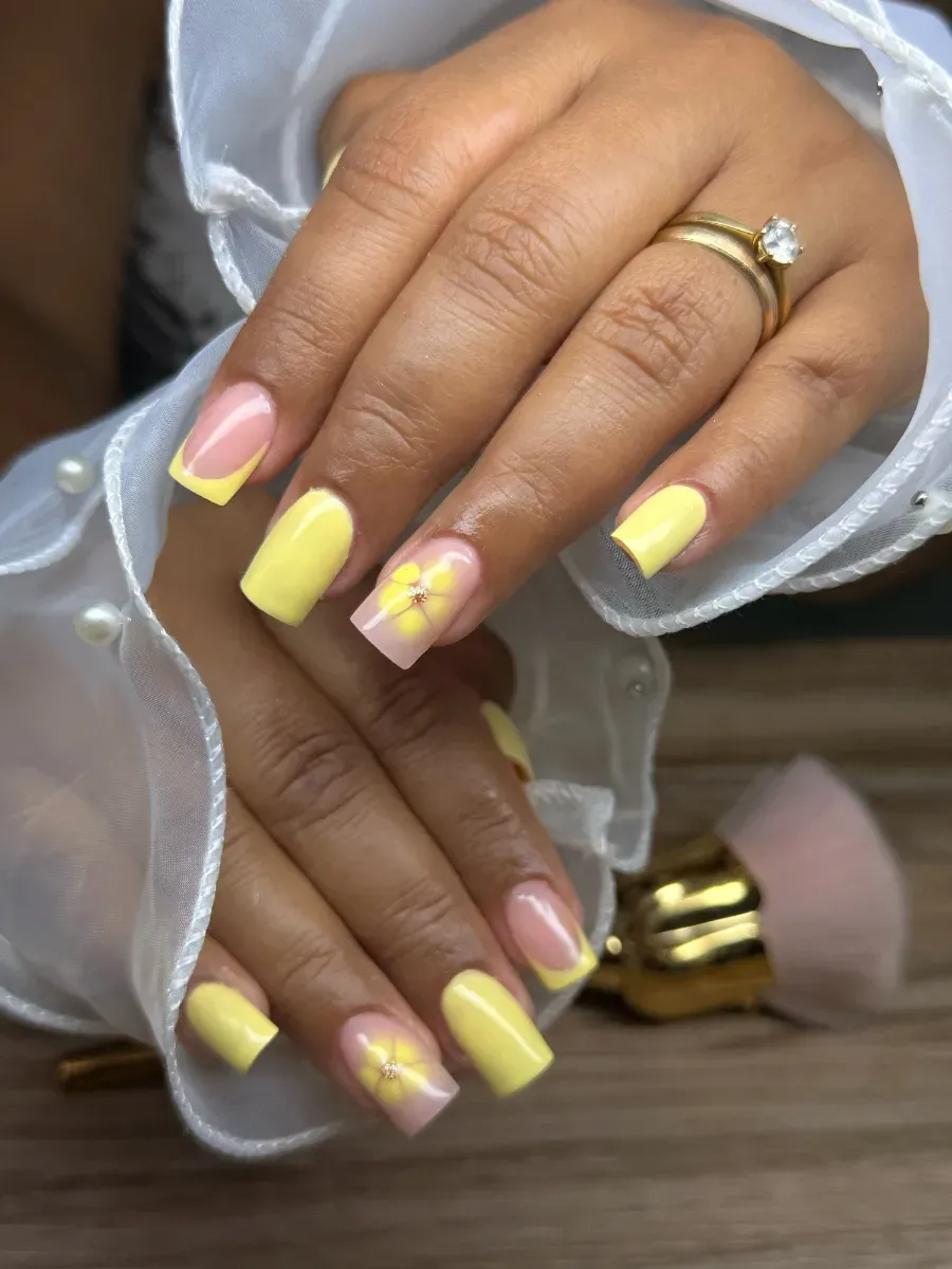 Manos con uñas pintadas en tonos amarillo pastel y rosa, que llevan anillos, descansando sobre una superficie de madera.
