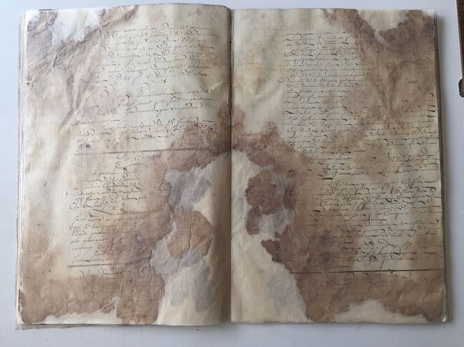 Livre ouvert, papier vieilli avec taches brunes et texte manuscrit.