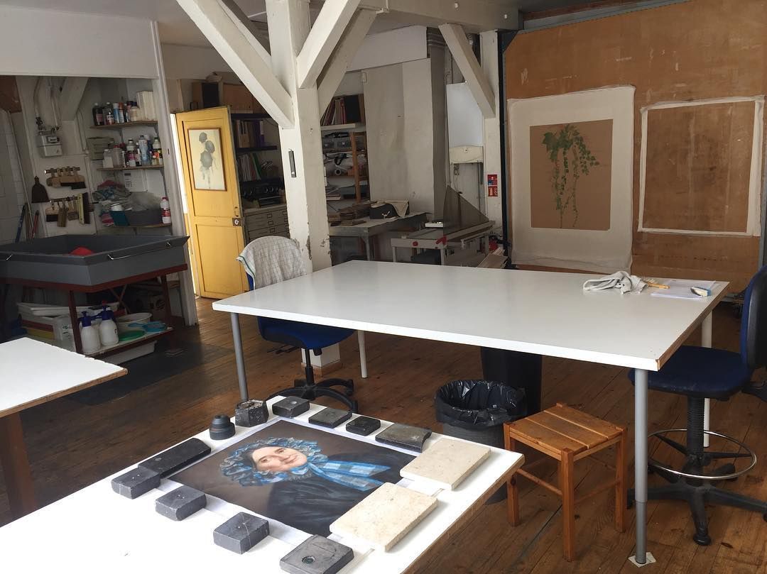Atelier d'artiste avec tables blanches, poutres en bois, tableaux et fournitures d'art.
