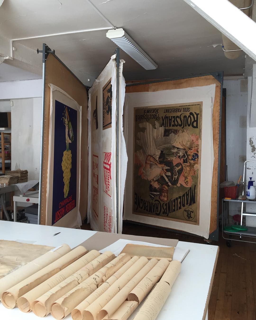 Grandes affiches vintage en stock, certaines montées, sur une table avec des documents roulés.