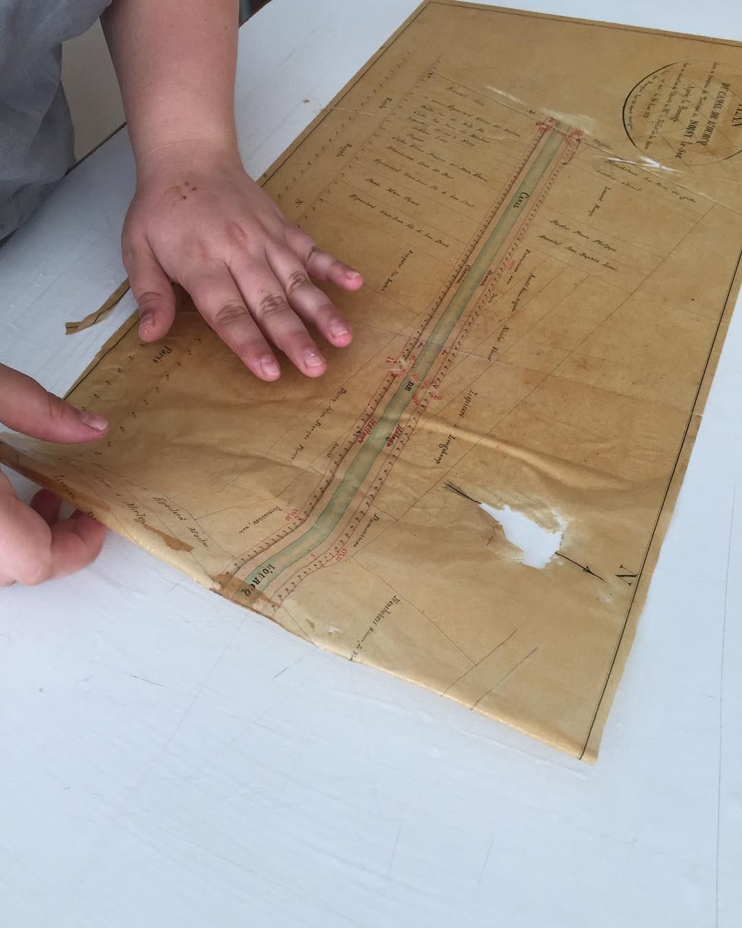 Mains tenant une enveloppe usée et beige sur une surface blanche avec un trou et des détails imprimés.