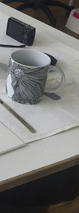 Une tasse avec un motif floral, une cuillère, un stylo et un appareil photo sur une surface blanche.