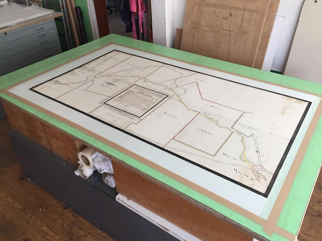 Une grande table avec une carte ancienne sous un plateau en verre, bordée de vert.