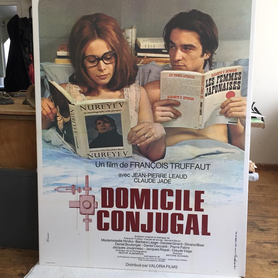 Affiche d'un film avec un couple au lit lisant un livre. Texte rouge et blanc.