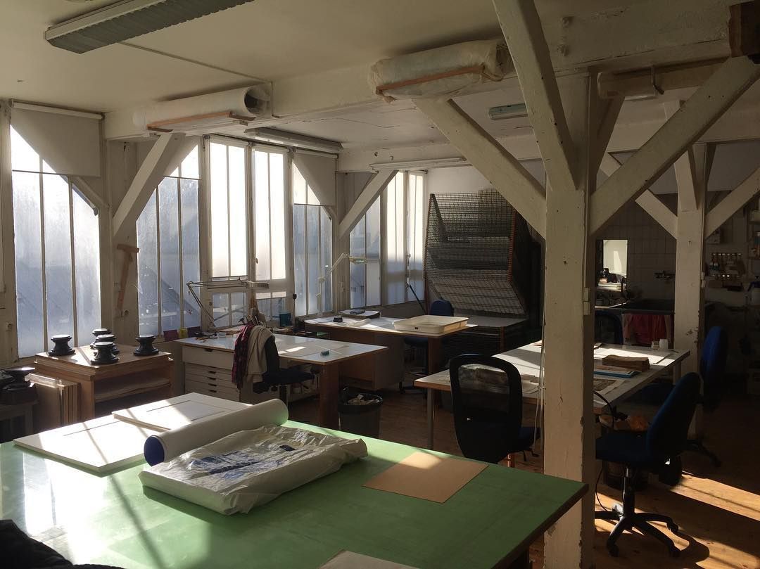 Intérieur lumineux avec tables à dessin, poutres en bois et grandes fenêtres.