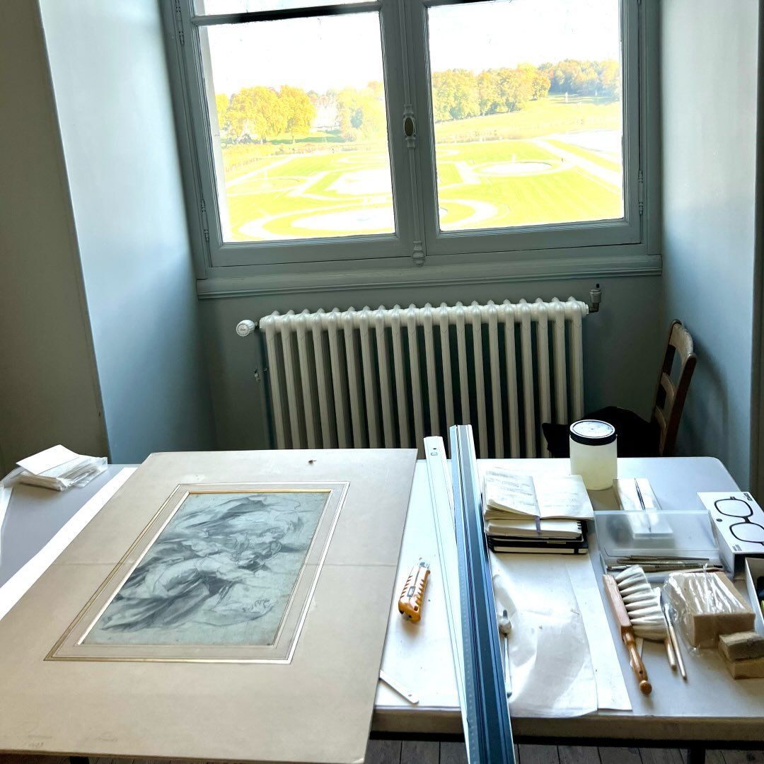 Un dessin sur une table près d'une fenêtre donnant sur un parc ; une pièce avec un radiateur et des fournitures d'art.